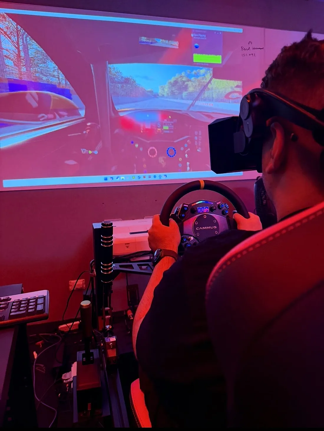 Driver gripping a direct drive wheel facing a racing sim screen